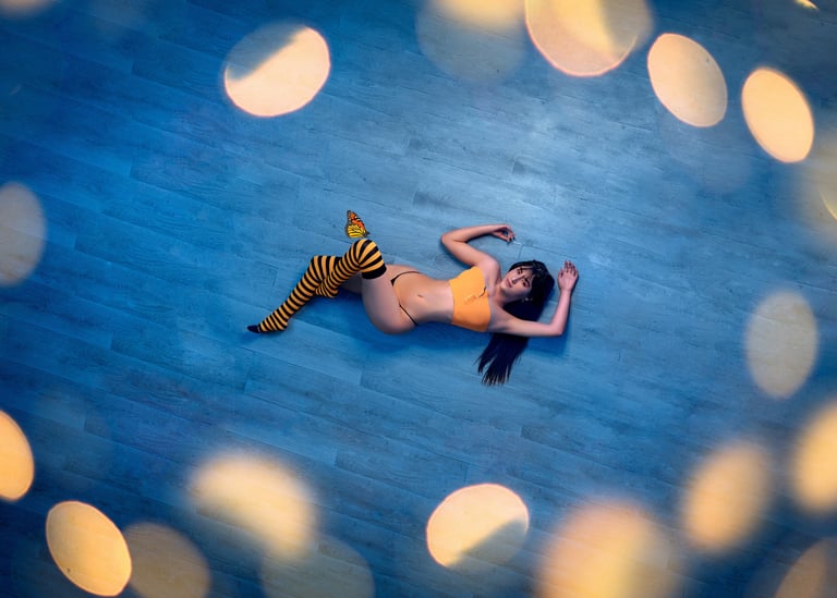 Woman in orange top and bee-striped socks lying on blue floor with glowing bokeh lights.
