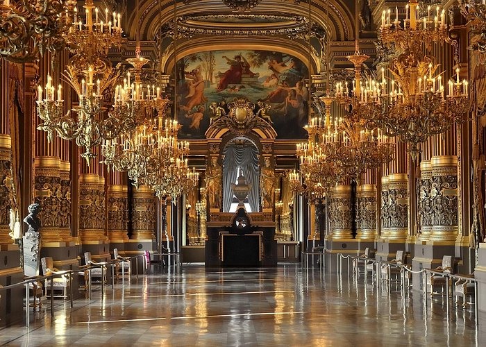Opulent Grand Foyer of the Palais Garnier opera house in Paris featuring ornate gold chandeliers and ceiling frescoes.