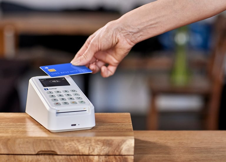 Customer making a contactless credit card payment on a SumUp card reader terminal at a shop counter.