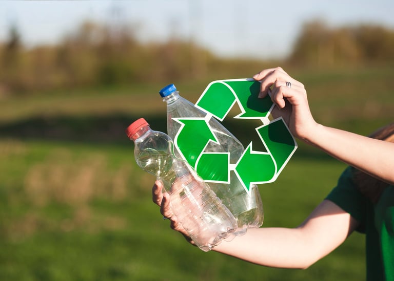 A person holding plastic water bottles and a green recycling symbol outdoors to promote sustainability.