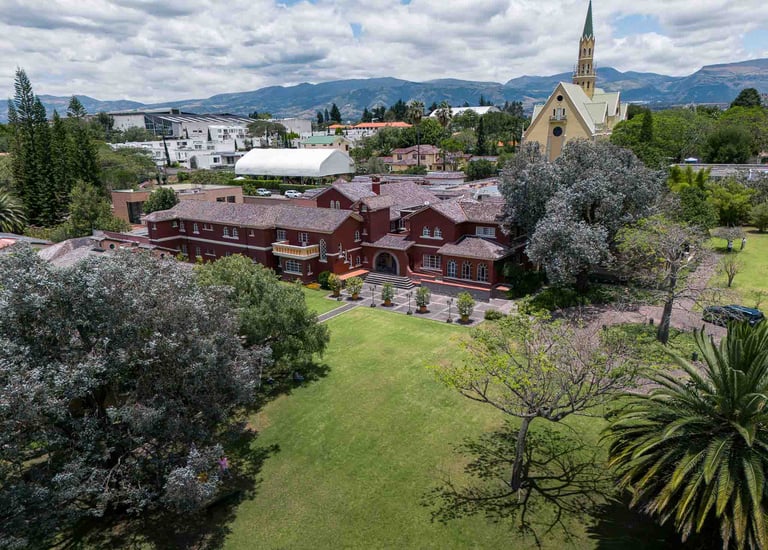 Fotografía aérea de gran casa religiosa de color rojo rodeada de hermoso  jardín verde en Quito Ecuador