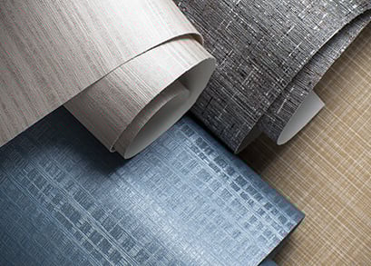 Close-up of textured wallpaper rolls in neutral tan, grey, and blue crosshatch patterns.