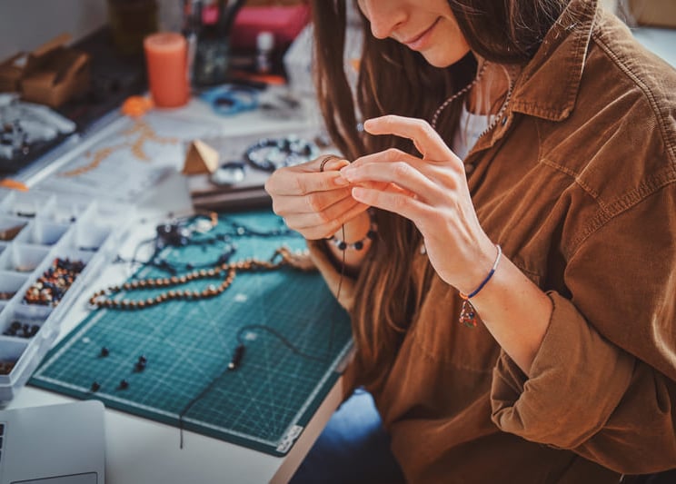 Un joyero elabora un collar hecho a mano con cuentas en un escritorio de taller con herramientas.