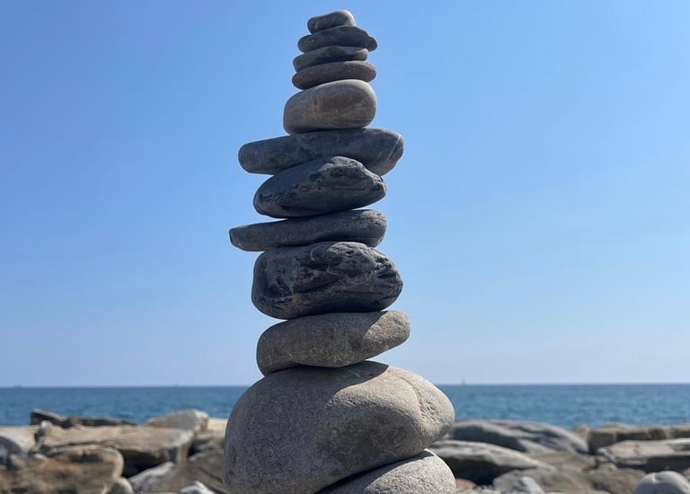 des galets empilés pour former un cairn avec en fond la mer et le ciel bleu