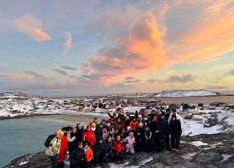 a group of people standing on a rocky cliff with a beautiful pink sky in the nordics