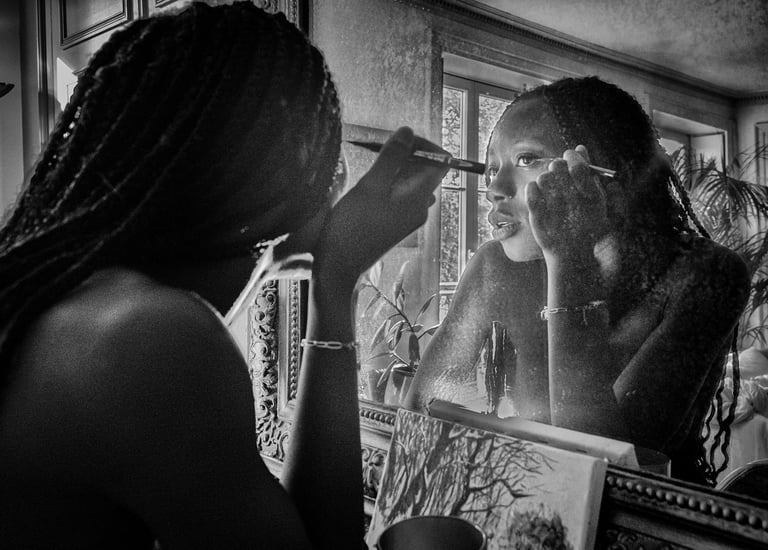 Photo artistique noire et blanc d'une jeune femme noire qui se requi se remaquille dans le miroir d'un intérieur haussmannien