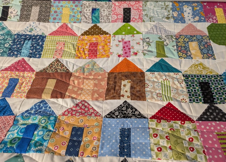 Patchwork quilt with colorful house blocks, each featuring patterned roofs and doors.
