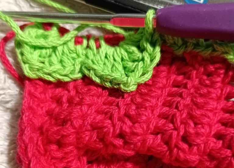 Primer plano de un proyecto de crochet de fresa roja y verde hecho a mano con un ganchillo morado.