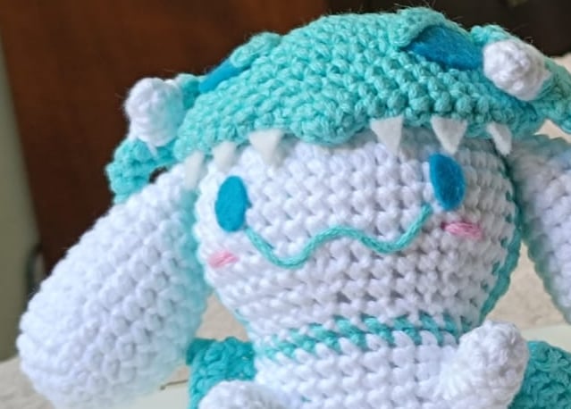Dos peluches Cinnamoroll tejidos a mano, uno de ellos con un disfraz de dragón verde azulado.