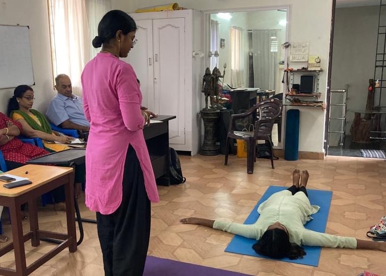 a woman in a pink shirt is standing in a room with several people during a teacher yoga class