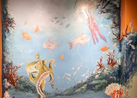 An active, life filled colorful coral reef of fish, octopus, and jelly fish wall mural by Kathy LaFollett.