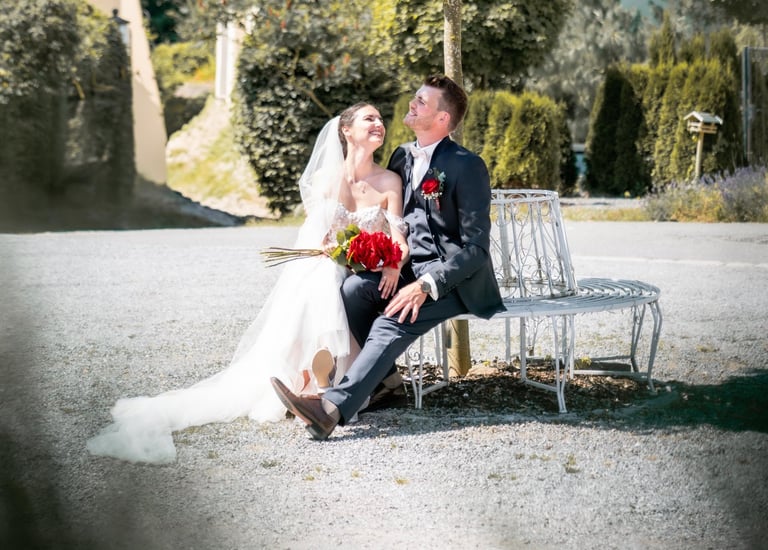 a bride and groom sitting on a bench in a park