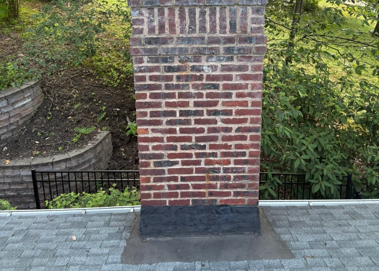 A brick chimney on a brown tiled roof with smoke rising from it, illustrating a safe and active fireplace system