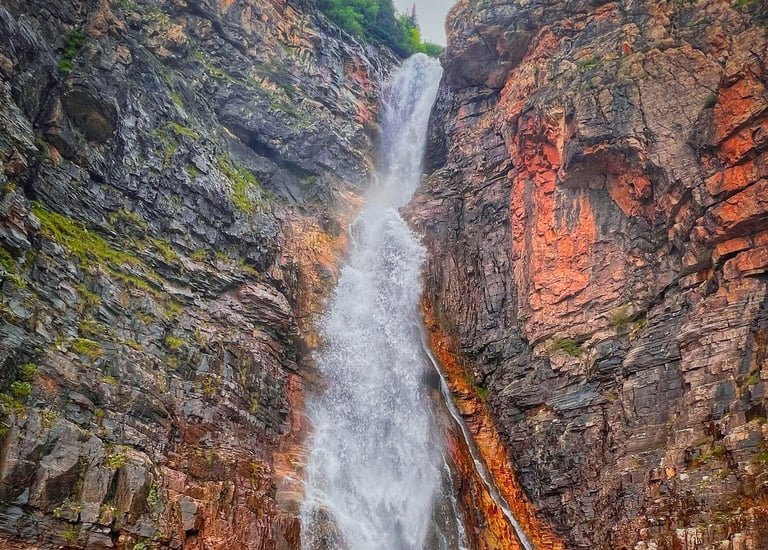 Scenic waterfall cascading down a rugged mountain cliff into a rocky stream in the wilderness.