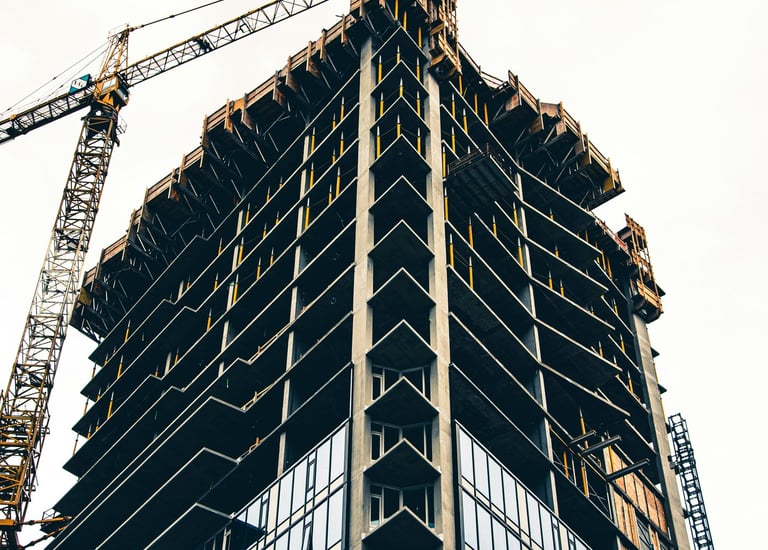 Low angle view of a modern skyscraper under construction with a yellow tower crane against a bright sky.