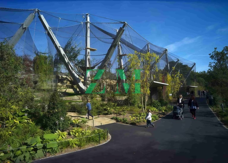 Visitors walk past the Snowdon Aviary walk-through exhibit at London Zoo under a clear blue sky.