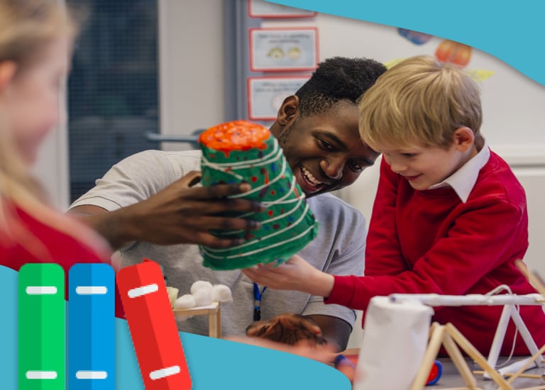 Smiling teacher helps elementary student with a colorful science volcano project in a classroom.