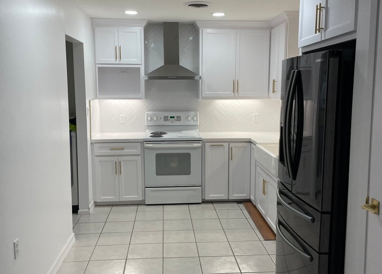 Modern white kitchen with shaker cabinets, gold hardware, and a black refrigerator.