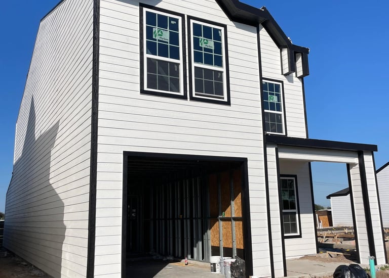 A modern two-story house under construction with white horizontal siding and black window trim.