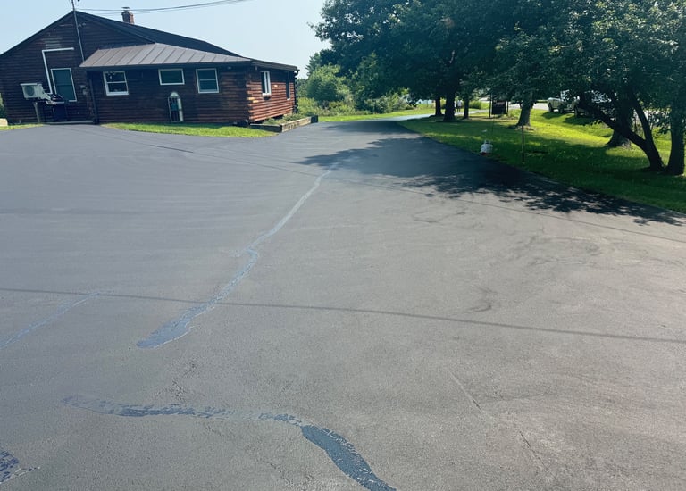 Freshly sealed asphalt driveway with crack filler next to a rustic log cabin home.
