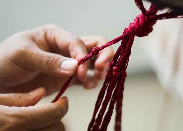 Manos realizando nudos intrincados con hilo rojo para un proyecto textil tradicional.
