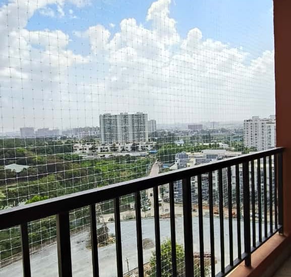 Close-up of a sturdy safety net securing a balcony with a view of Coimbatore skyline.