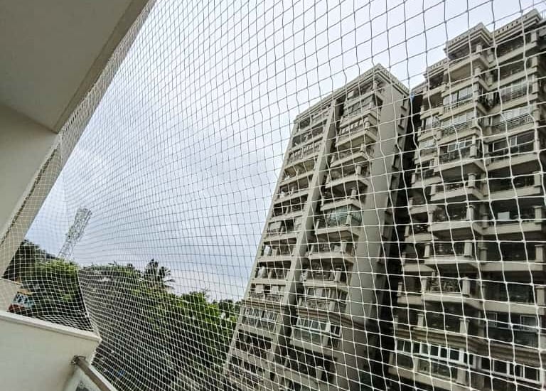 Technician carefully fitting a safety net on a balcony railing.