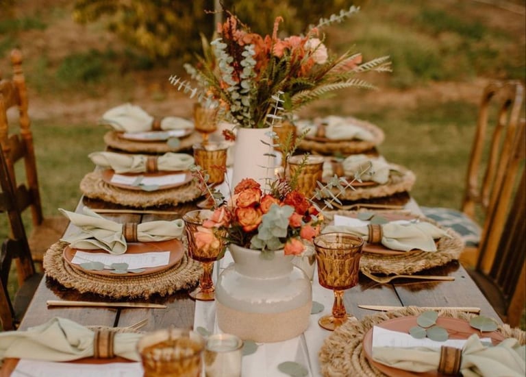 Mesa rústica de boda con platos apilados y centro floral otoñal.