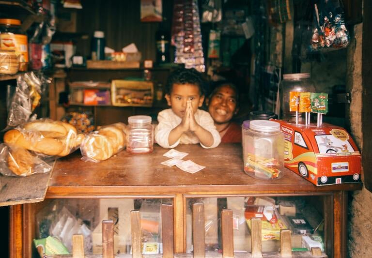 A young child and mother smiling behind the counter of a small local grocery shop.
