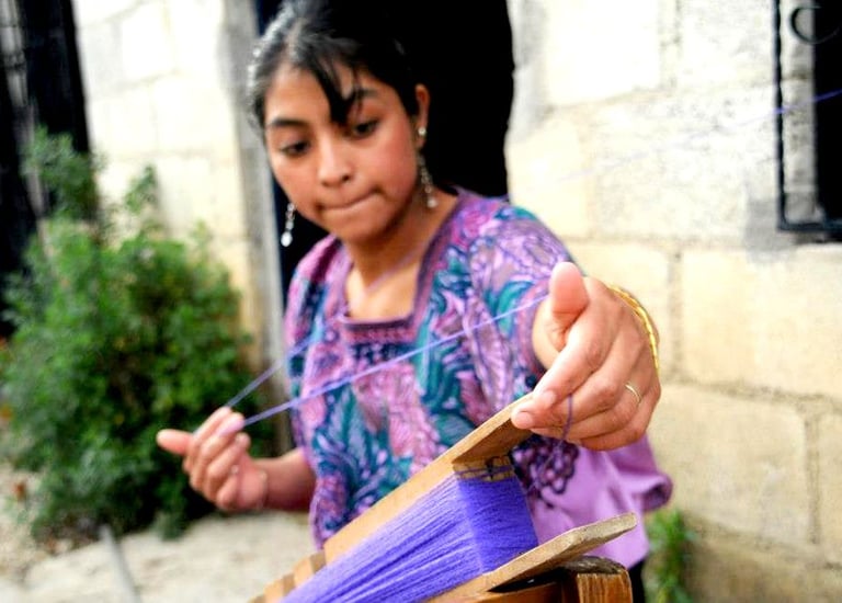A skilled artisan weaver in Guatemala handcrafting textiles with purple yarn on a traditional loom.
