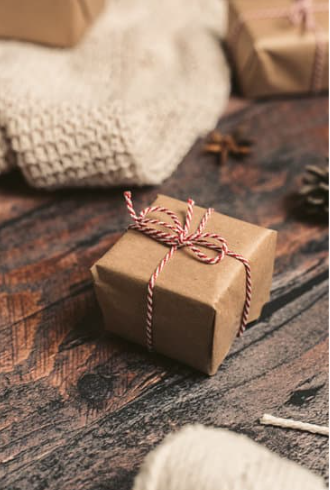Small brown paper gift box tied with red and white twine on a rustic wooden table.