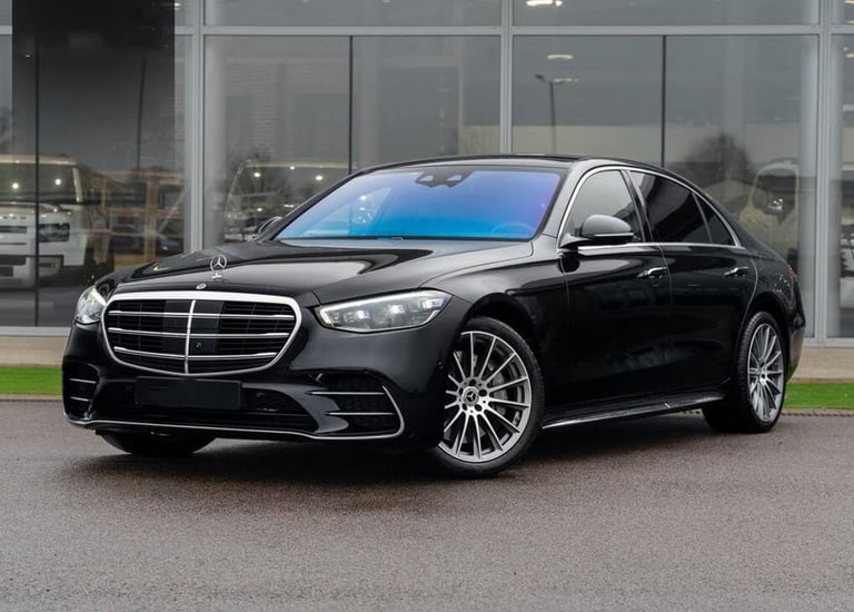 Luxurious black Mercedes-Benz S-Class sedan parked outside a modern car dealership showroom.