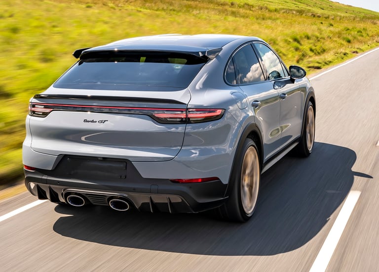 Rear view of a grey Porsche Cayenne Turbo GT driving fast on a scenic mountain road.