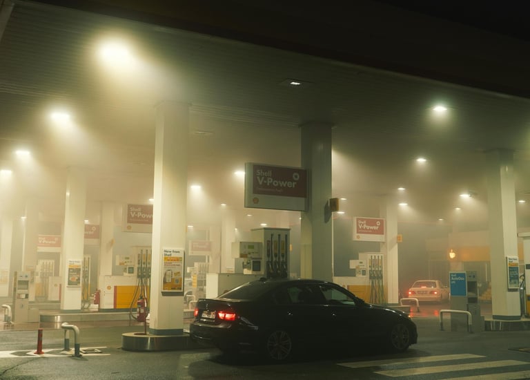 A dimly lit Shell gas station in Chichester, England, with fog or smoke hanging in the air, a black