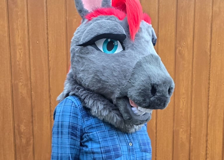 Grey horse fursuit head with red hair and blue eyes, worn with a blue plaid shirt.