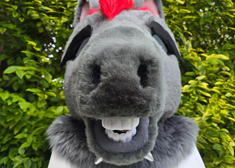Custom grey furry horse head mask with red mohawk and realistic teeth displayed outdoors.