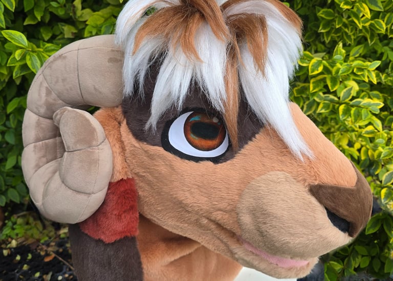 Handmade brown and white ram fursuit head with curved ram horns and faux fur mohawk.