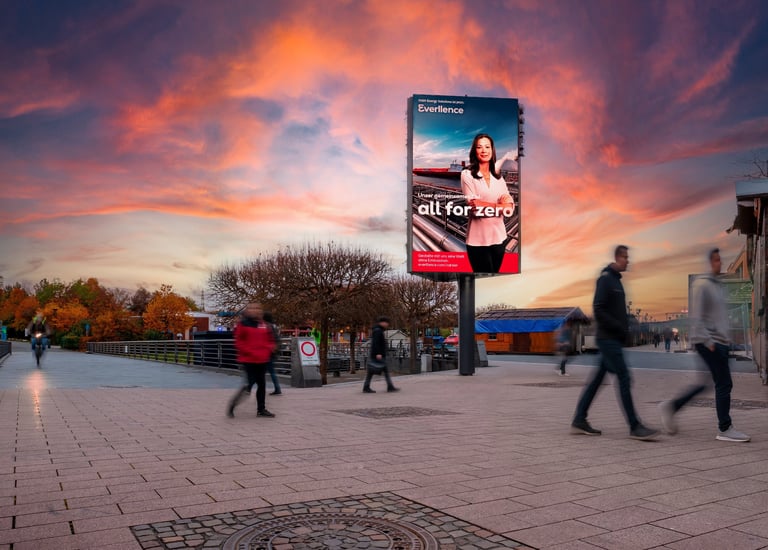 Digital billboard advertising renewable energy campaign in a city plaza under a vibrant sunset sky.