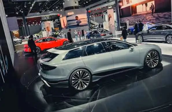 A slick, modern exhibition space featuring several high-end cars. A white sedan is prominently displ