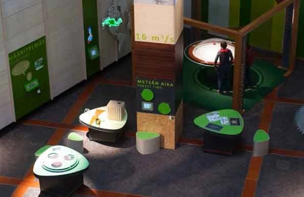 A modern exhibition space featuring interactive displays and informational panels predominantly in g