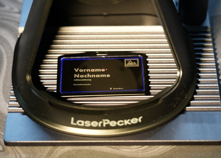 A LaserPecker engraving machine personalizing a black metal business card with custom text.