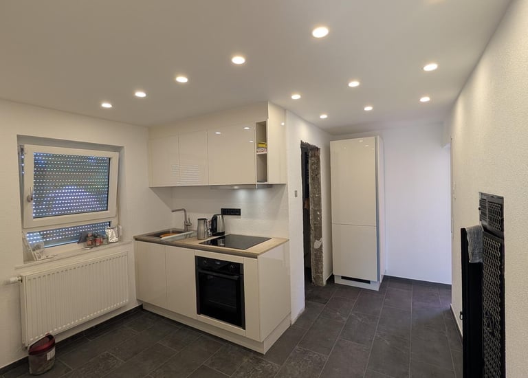 eine sanierte weiße Küche mit Deckenspots, grauen Fliesen auf dem Boden.