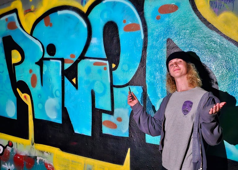 young person standing in front of a mural with Reid's name