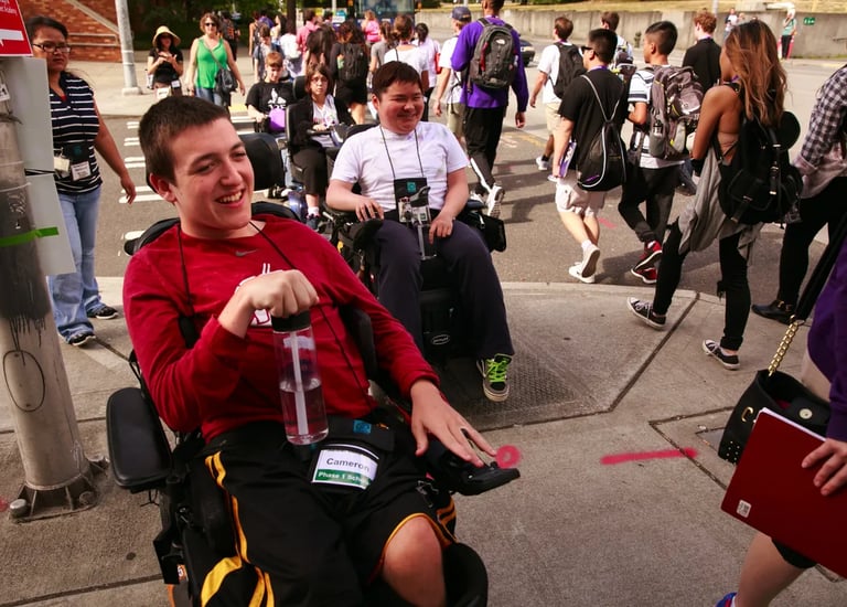 Two young men in power wheelchairs smiling as another group of people walks away from camera