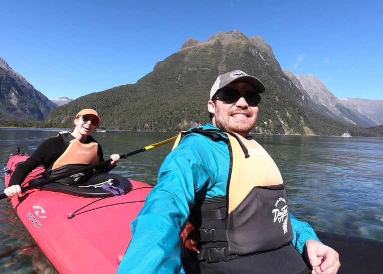 Sean wearing a teal jacket and ball cap in a kayak in New Zealand's Milford Sound