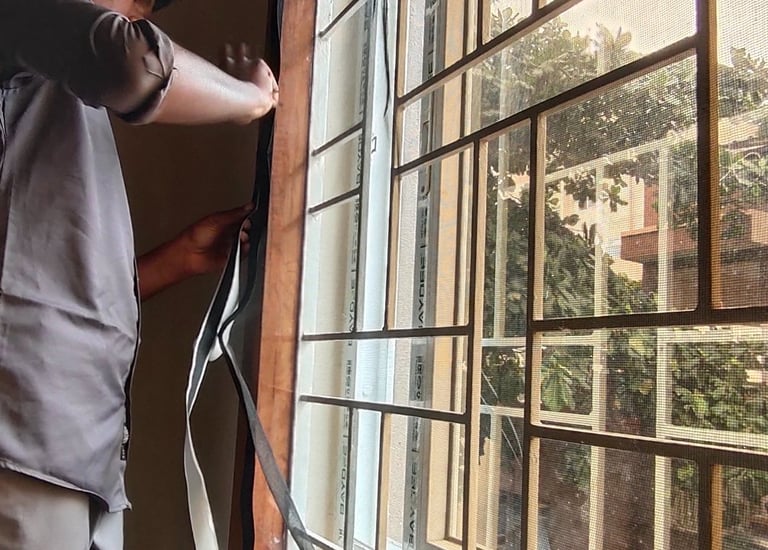 A washable velcro mosquito net being gently removed from a metal window frame for cleaning.
