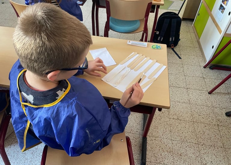 Image d'un élève en activité individuelle qui peint des bâtonnets de bois