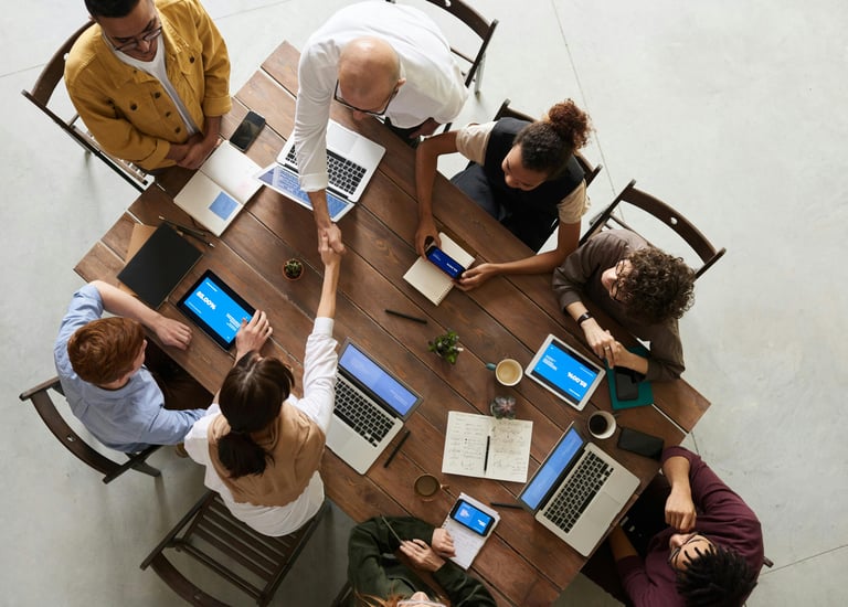 a group of people sitting around a table with laptops