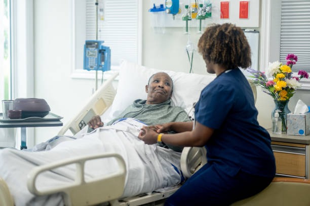A nurse converses with an elderly man resting in a hospital bed, providing care and support during h