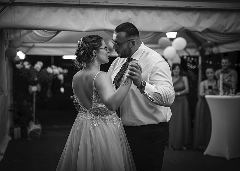 Ein Schwarz-Weiß-Foto eines Brautpaares, das bei seiner Hochzeit tanzt, wobei die Braut ein rückenfreies Kleid trägt und der